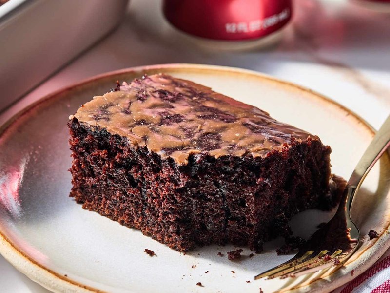 A piece of chocolate cake on a plate with a fork background shows blurred drink cans