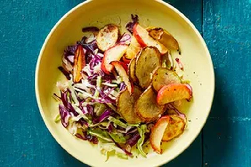 A bowl of slaw with apples and potatoes on a blue surface