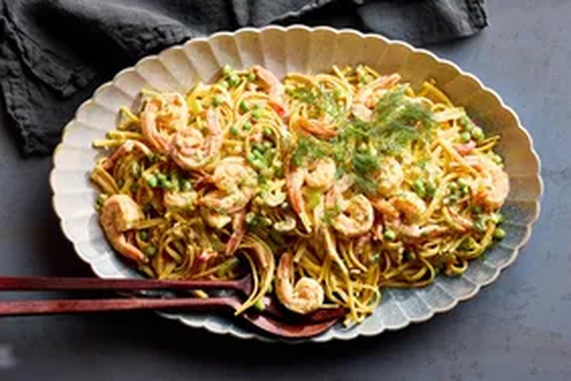 A cold shrimp linguine pasta salad served on an oval dish with garnish and utensils