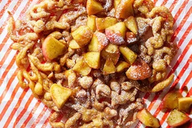 A funnel cake topped with apple slices and powdered sugar