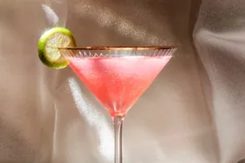 A martini glass with a pink drink and a lime slice garnish