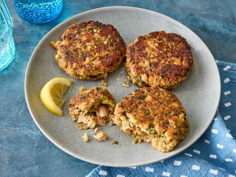 A plate with three salmon cakes, served with a lemon wedge