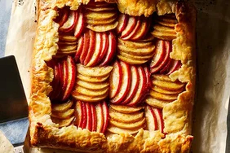 A rustic caramel apple tart with a puff pastry crust and neatly arranged apple slices on parchment paper