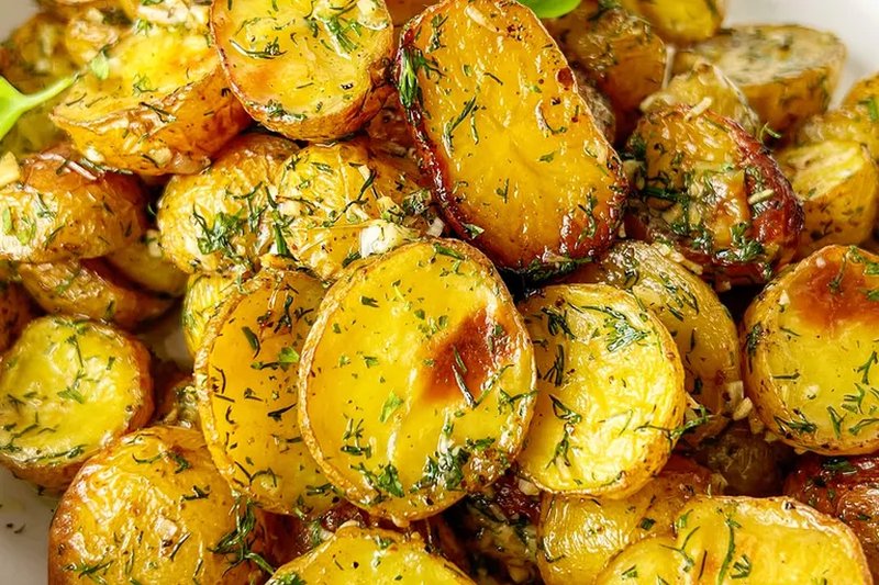 A serving of roasted potatoes seasoned with diced dill and garlic closeup view