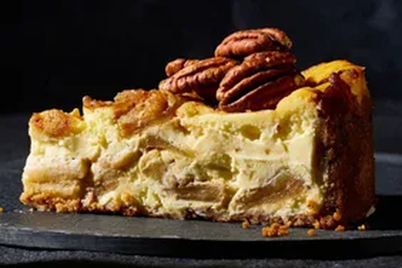 A slice of caramel apple brandy cheesecake topped with pecans