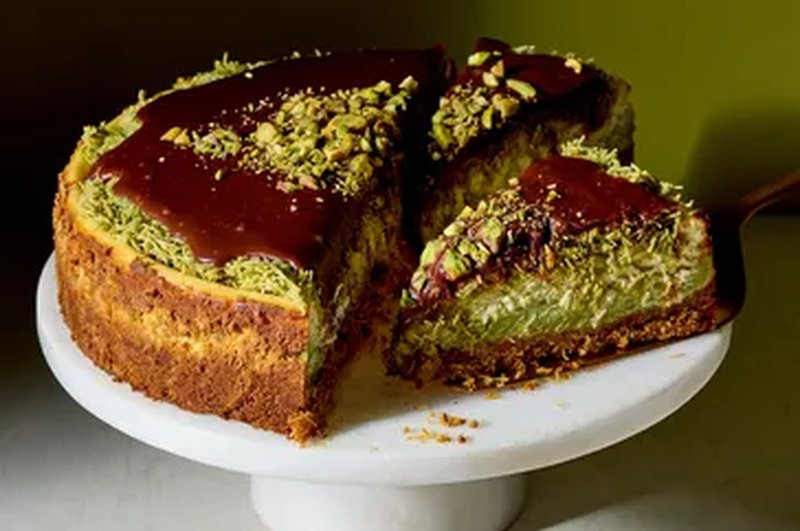 A sliced pistachio cheesecake with chocolate topping displayed on a cake stand