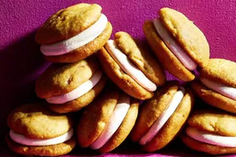 A stack of apple whoopie pies with cream filling arranged against a pink background