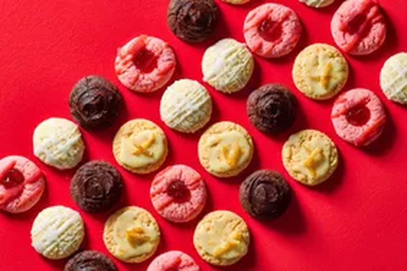 An assortment of cookies arranged on a red background featuring a variety of types and decorative toppings