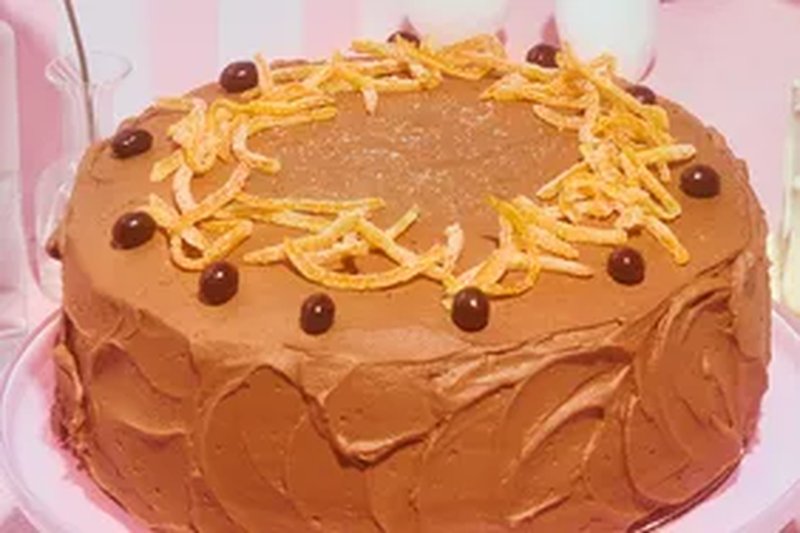 chocolate frosted layer cake on pink pedestal with orange peel and espresso bean decoration