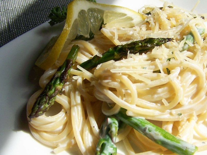 Close-up view of creamy asparagus pasta garnished with cheese and a lemon slice on a white plate