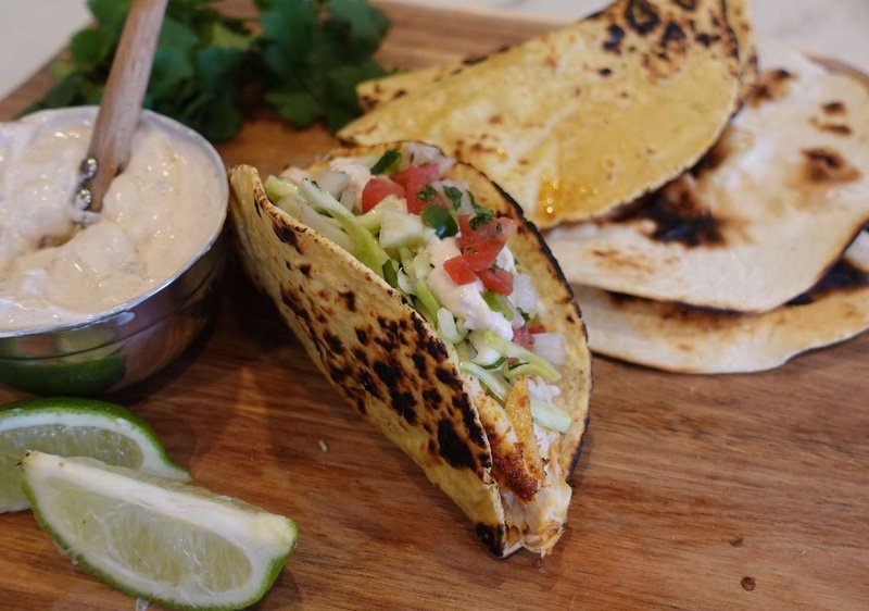 Fish taco topped with cilantro slaw on a wooden cutting board