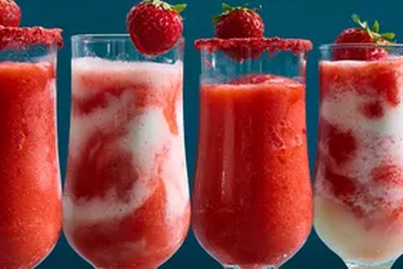Four glasses of frozen strawberry daiquiris some garnished with whole strawberries