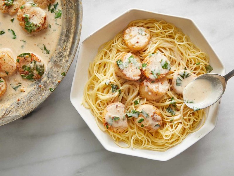 overhead view of scallops over spaghetti in a large white bowl, with sauce spooned over pasta.
