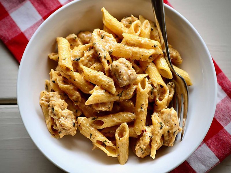 overhead view of white bowl of penne with chicken in cowboy butter sauce on red check napkin