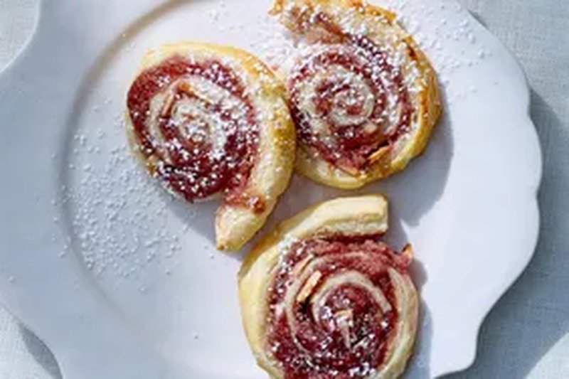Pastry pinwheels with raspberry filling and almond topping on a plate dusted with powdered sugar