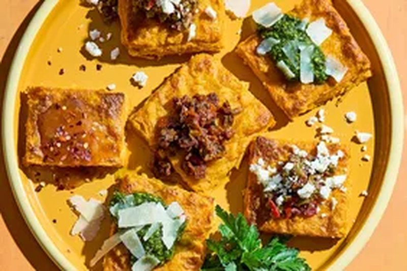 Plate of polenta squares with various toppings including cheese herbs and sauces