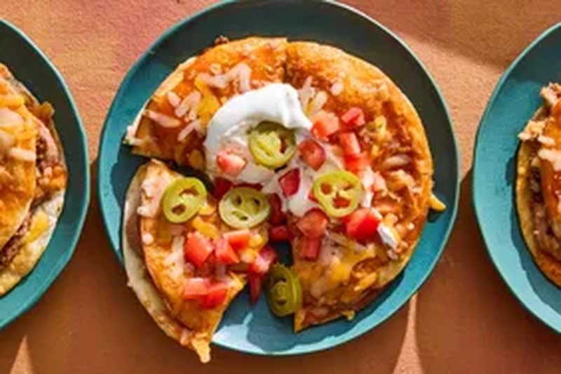 Plates of Mexicanstyle pizzas topped with ingredients such as melted cheese diced tomatoes jalapeo slices and a dollop of sour cream