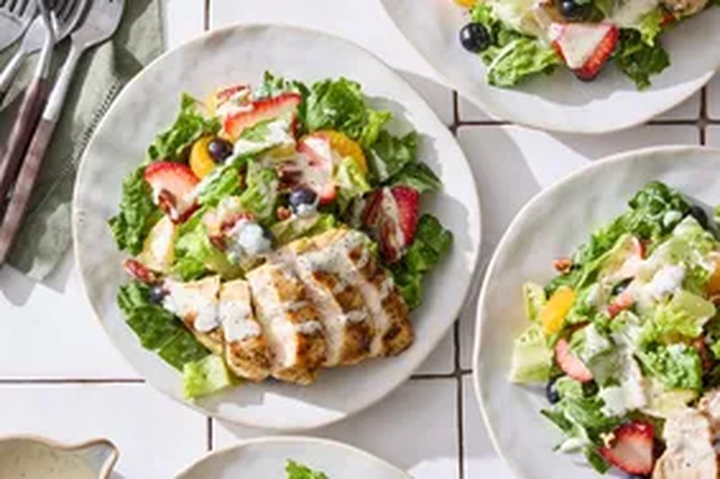 Plates of salad with sliced grilled chicken fruits and greens arranged on a table