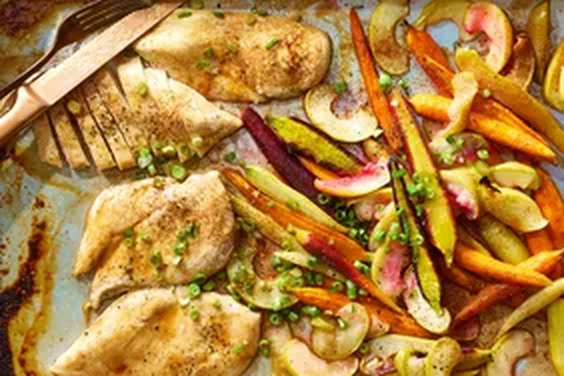 Sheet pan meal with baked chicken fillets roasted carrots and apple slices garnished with green onions