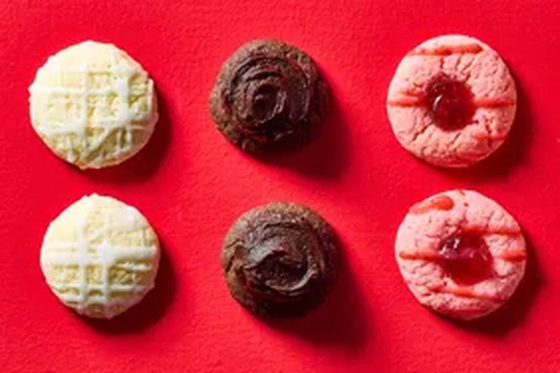 Six cookies arranged in two rows on a red background including wafflepatterned chocolate frosting topped and pink with jam cookies