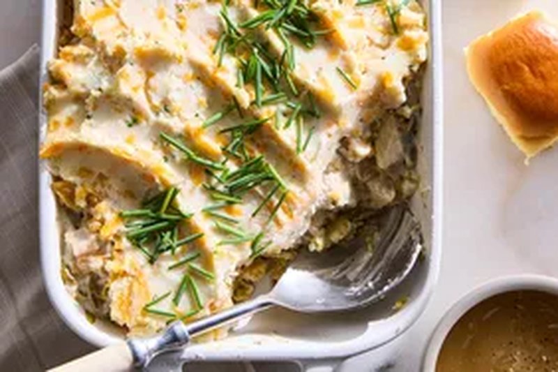 Thanksgiving casserole with a spoon garnished with herbs next to a dinner roll and sauce