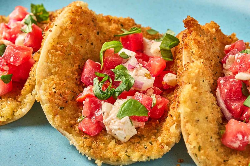 Three tacos with crispy shells filled with diced vegetables and herbs plated on a surface