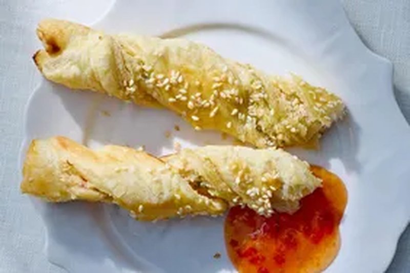 Two pastry twists with sesame seeds served on a plate with sweet chili sauce