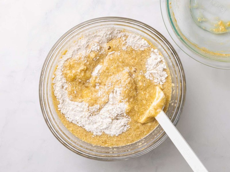 Banana bread batter being mixed in a glass bowl with a spatula