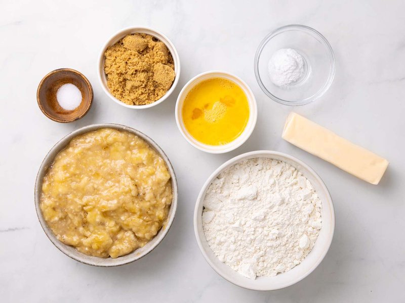 Ingredients for banana bread including mashed banana butter flour brown sugar egg mixture salt and baking soda